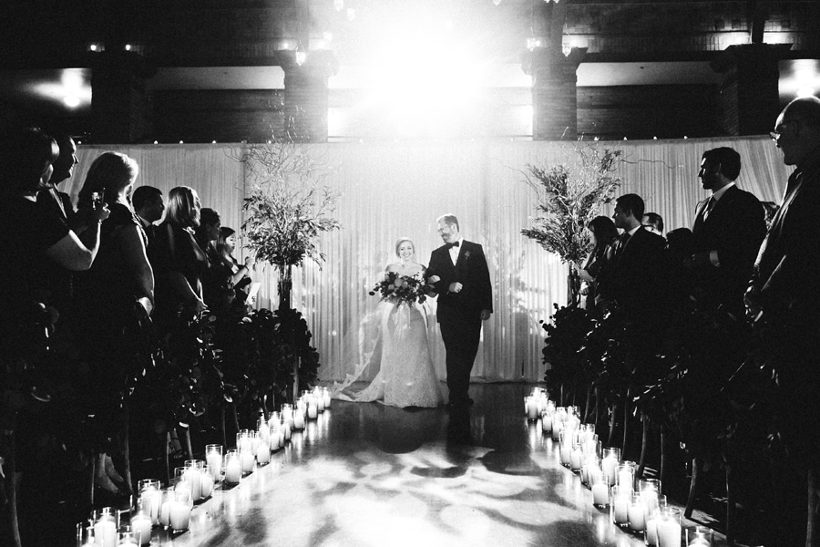 A bride is escorted by her father down a row of candles for her wedding ceremony.