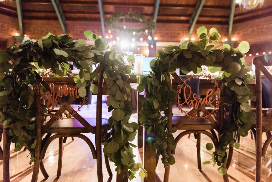 Custom bride and groom signs on the back of chairs with garland.