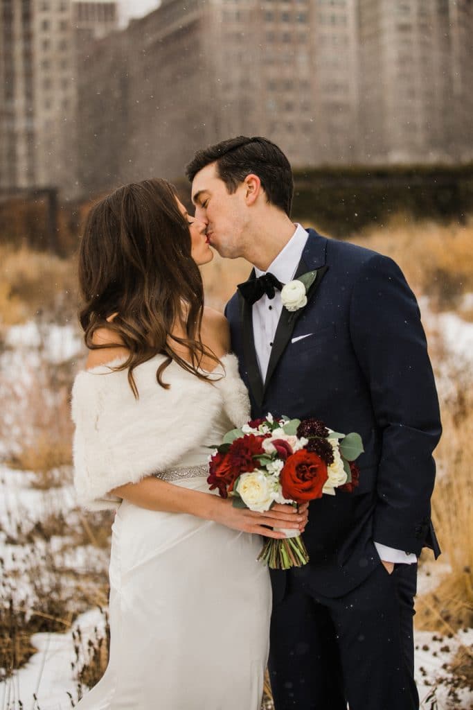 A bride and groom share a kiss as the snow begins to fall in Lurie Garden.