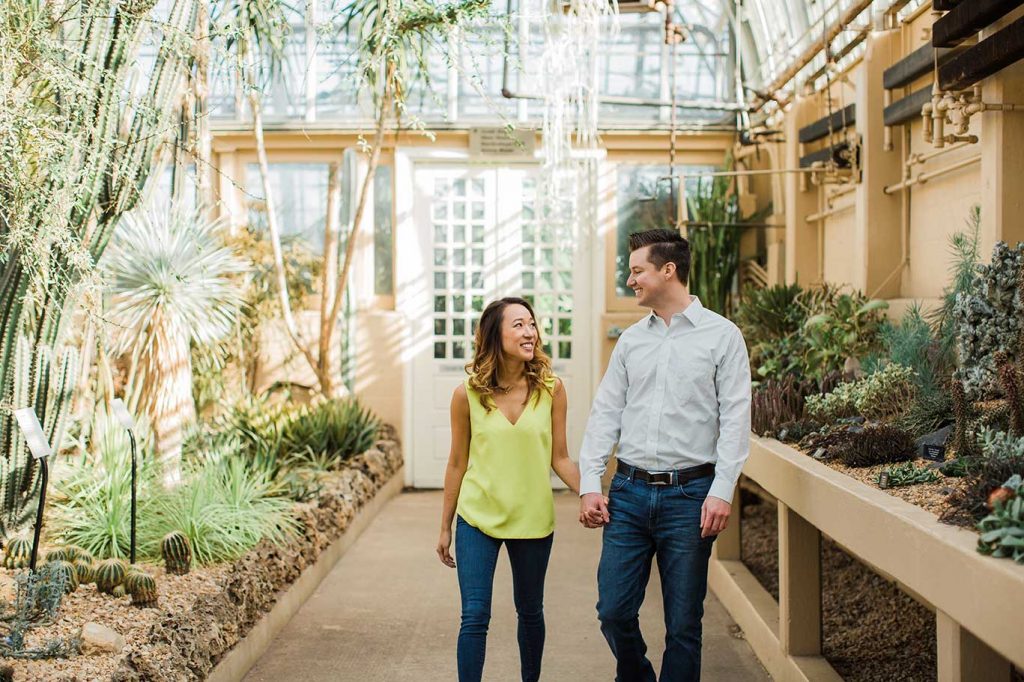 An engaged couple walks through Garfield Park Conservatory as they take indoor Chicago engagement photos