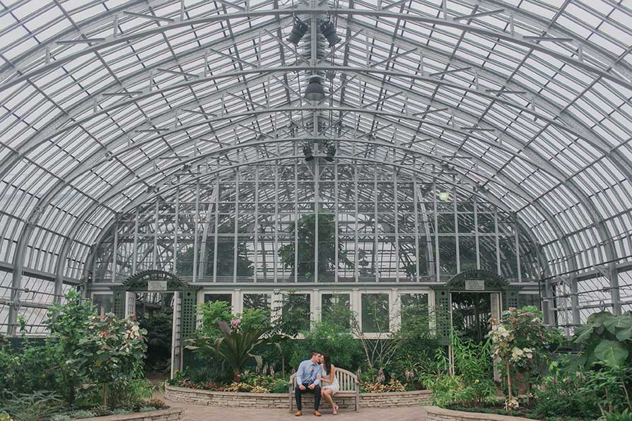 Engaged couple sharing a kiss while sitting on a bench at Garfield Park Conservatory.