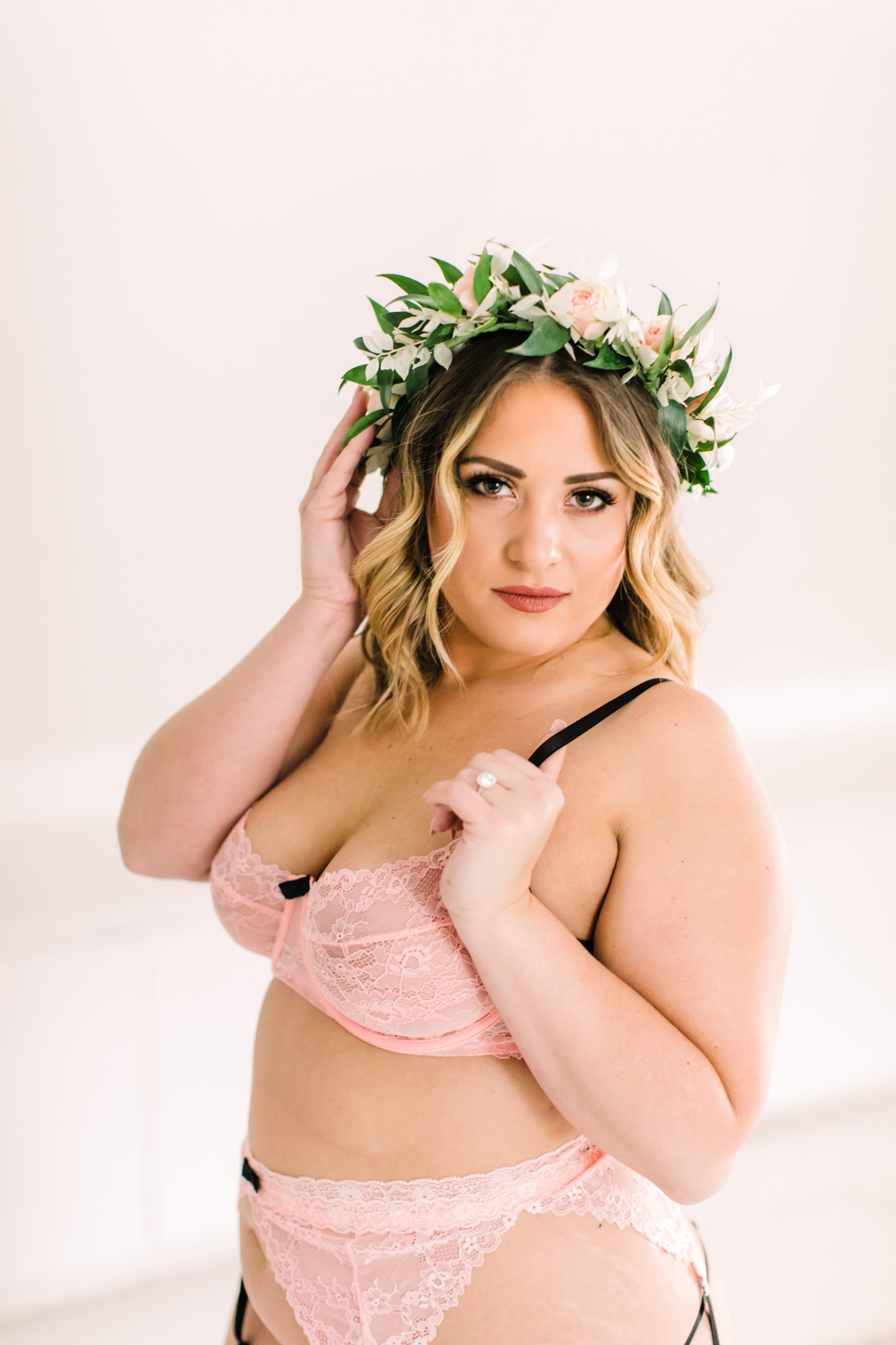 A woman poses while wearing pastel pink lingerie and a floral crown for her bridal boudoir session.