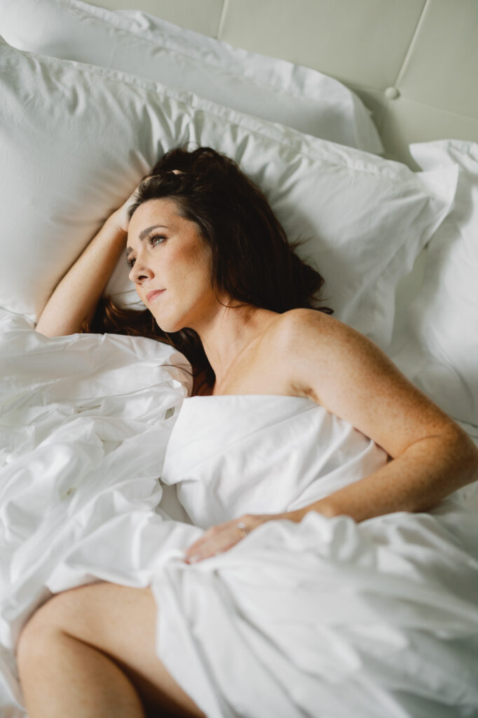 A woman poses in hotel bed sheets for her boudoir session