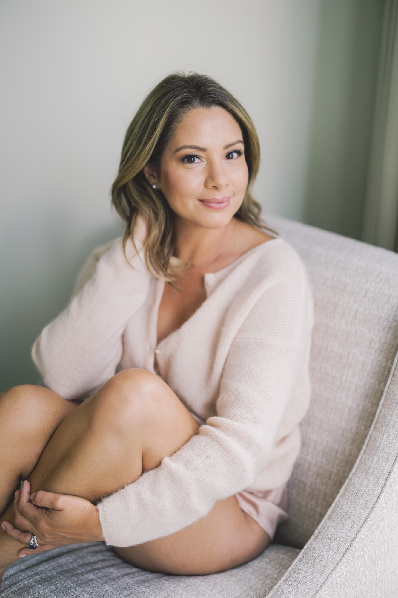 A woman poses for a boudoir photo while wearing a cozy pastel cardigan.