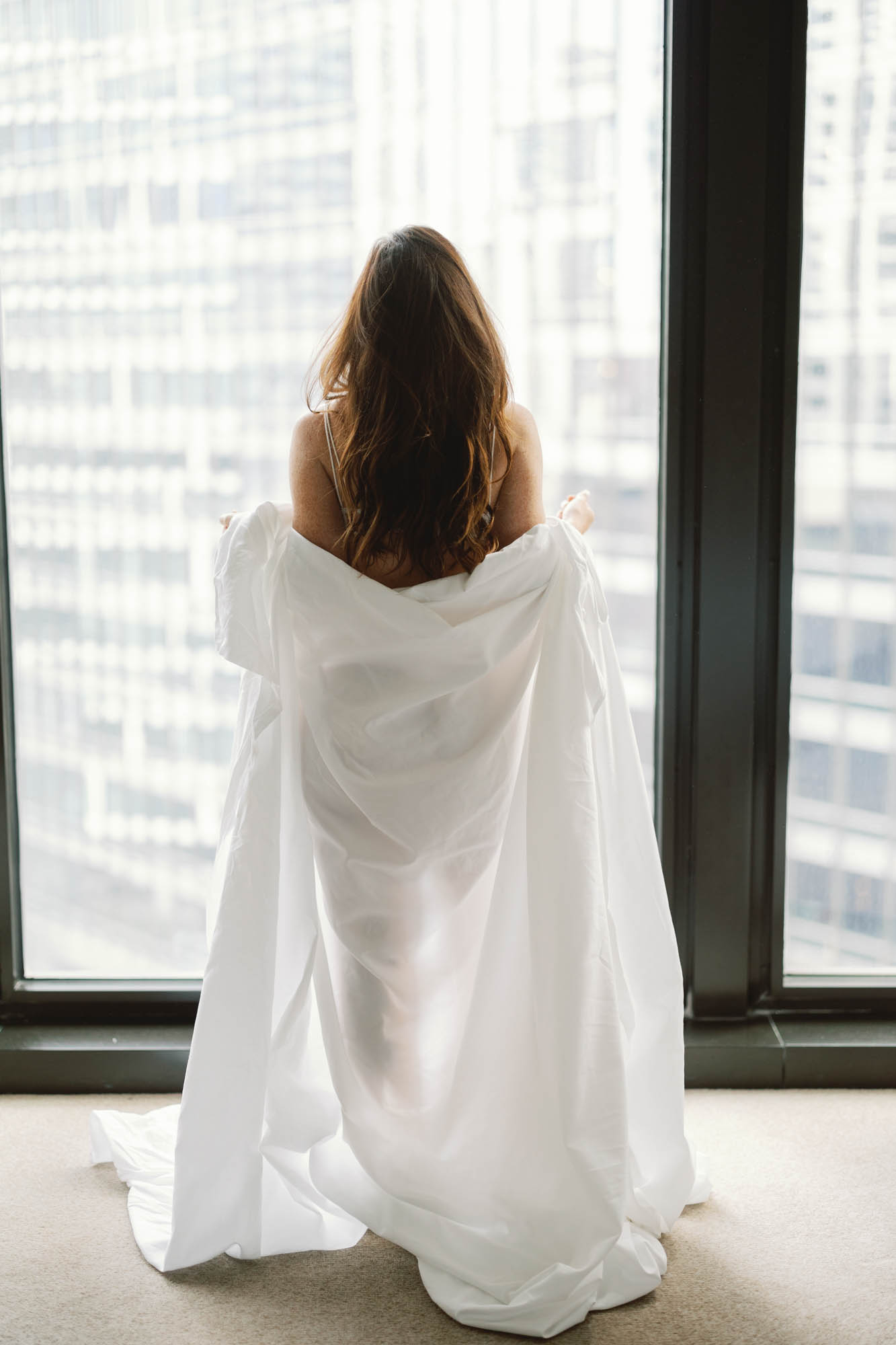A bride wrapped in hotel bed sheets poses for a boudoir session at the Langham Hotel in Chicago.