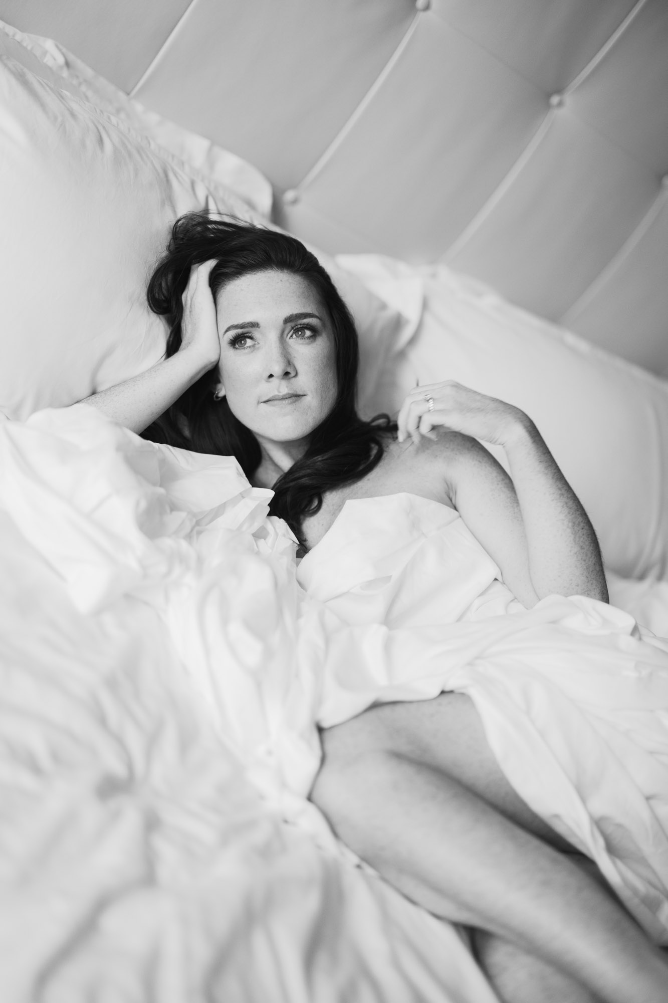 A bride poses in the sheets for her bridal boudoir hotel session.
