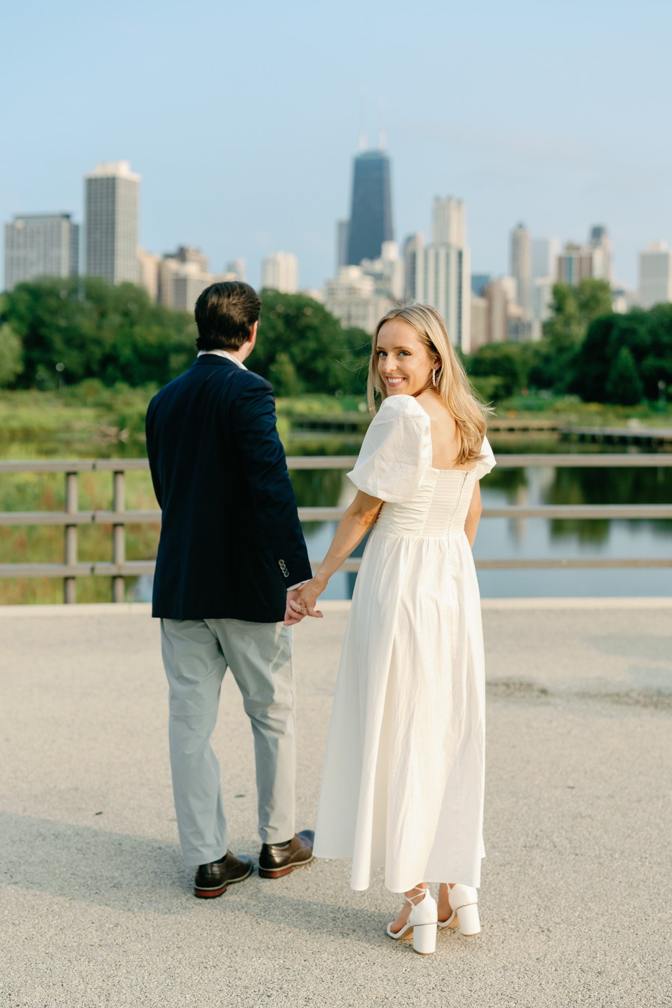 A bride smiles over her shoulder as she poses for an engagement photo with the Chicago skyline behind her.
