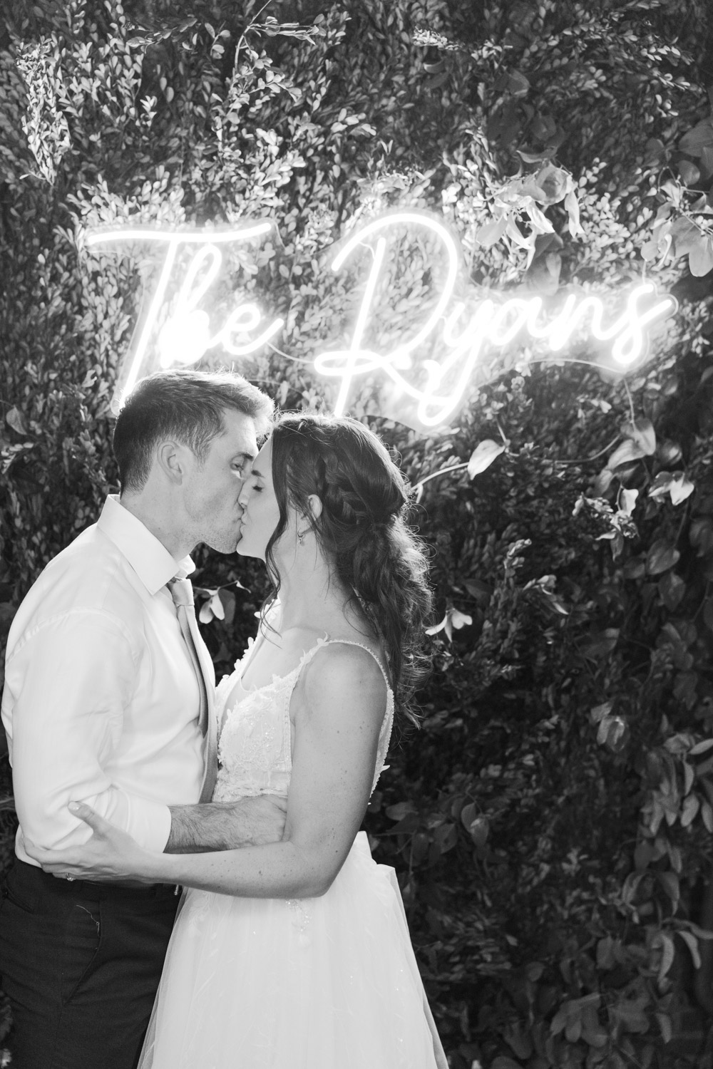 Bride and groom pose in front of custom neon sign on their wedding day