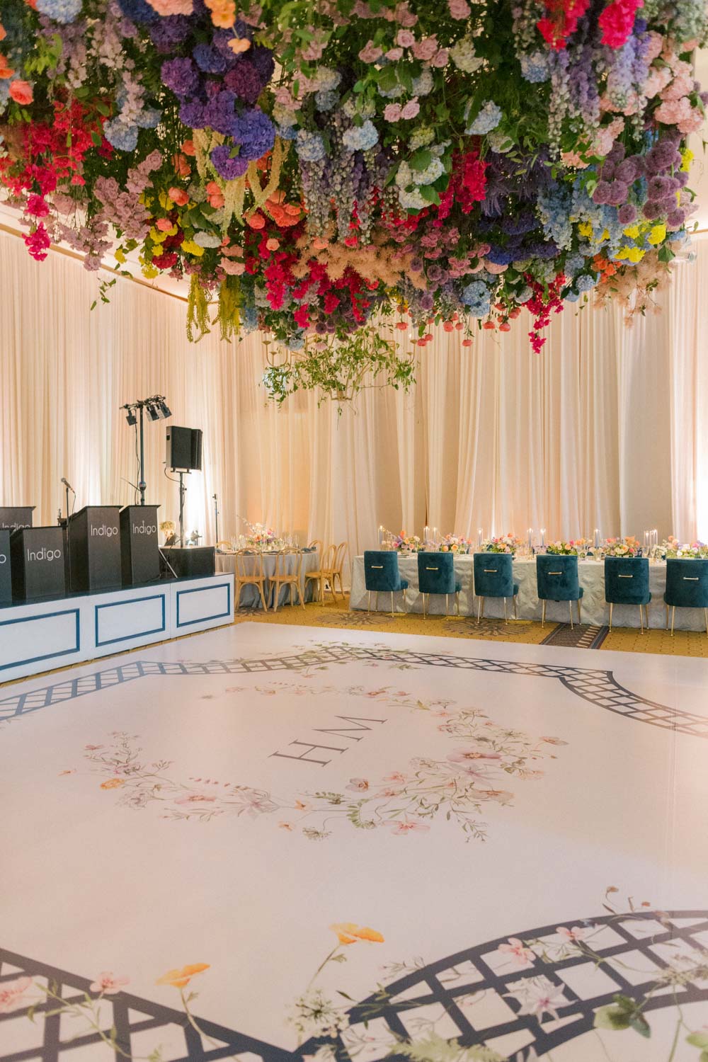 Colorful wedding flowers drape from the ceiling over a custom designed dance floor with the couple's monogrammed initials
