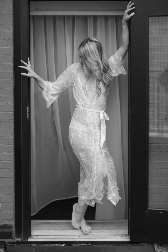 Woman in lace robe standing in doorway playful boudoir moment
