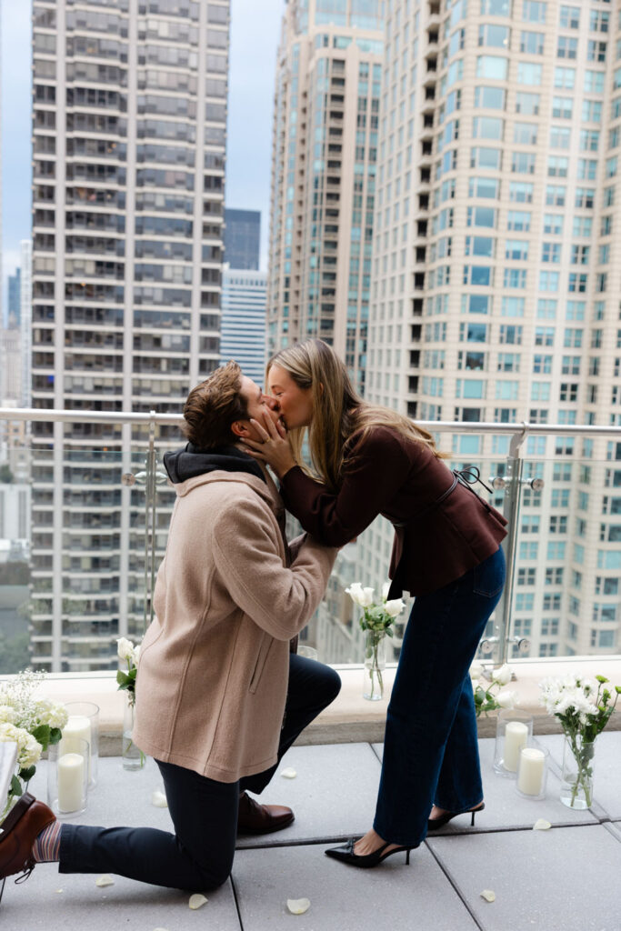 Man kneeling during a surprise rooftop proposal while his partner reacts with joy.