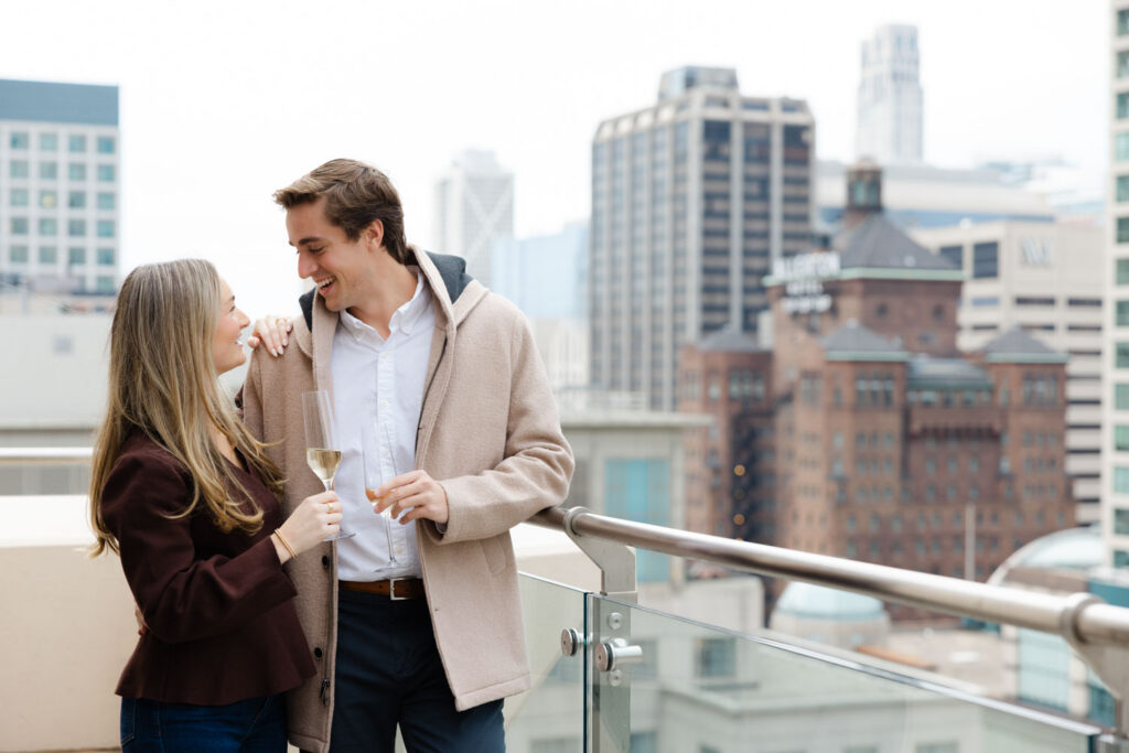 Couple toasting champagne while celebrating their engagement on a downtown Chicago rooftop.
