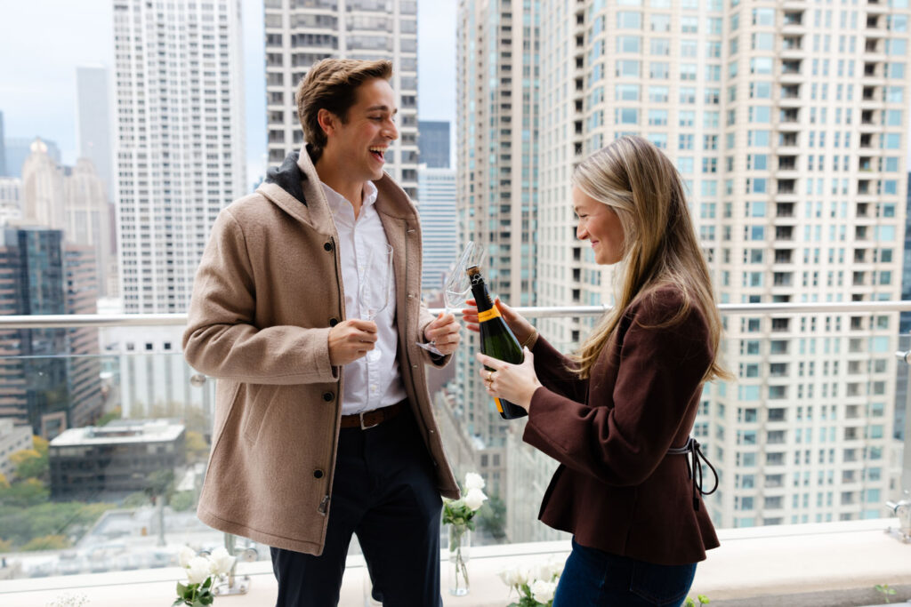 Newly engaged couple opening a bottle of Veuve champagne on a Chicago rooftop.