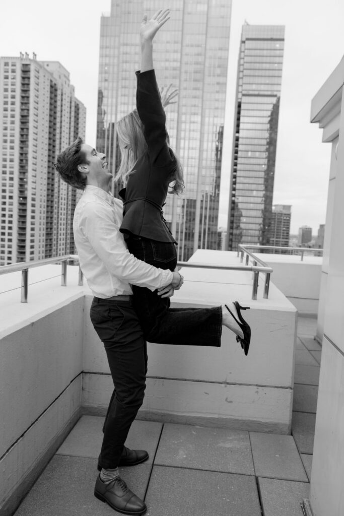 Woman jumping into her partner’s arms after proposal on rooftop in Chicago.