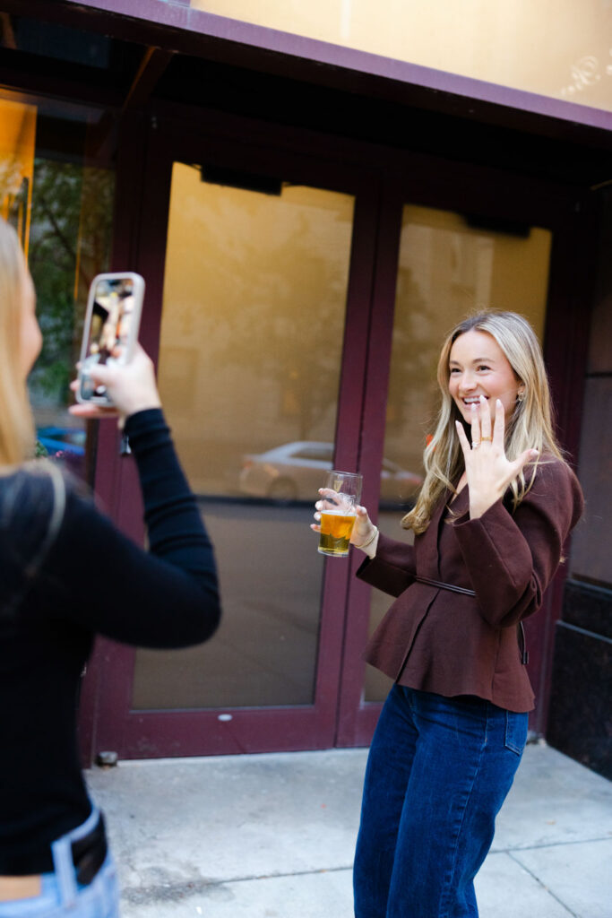 Newly engaged woman holding up her hand to show engagement ring outside Chicago bar.