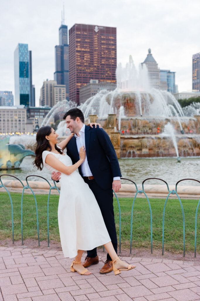 Couple embracing in front of Buckingham Fountain with Chicago skyline behind them
