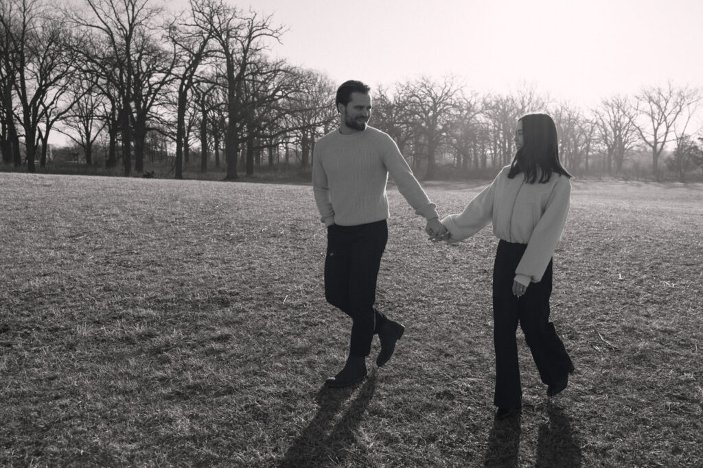 Black and white photo of couple walking hand in hand through open field