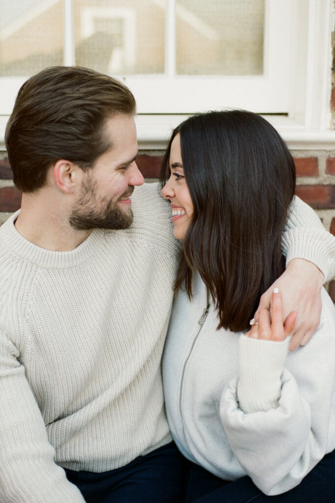 Couple sitting together outside brick building at Elawa Farm engagement session captured on film.