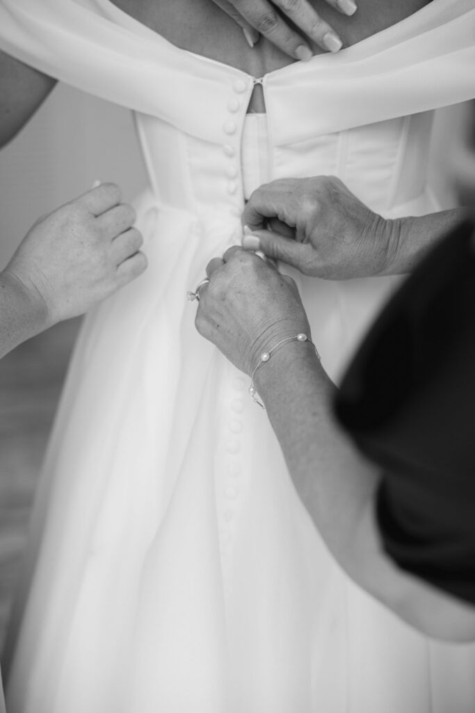 Bridesmaid fastening the back of the bride’s wedding dress