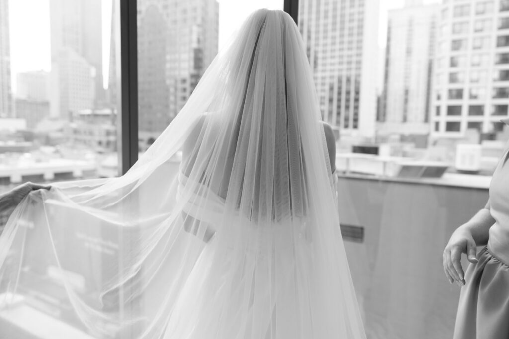 Bride’s veil flowing as she stands near a window overlooking Chicago