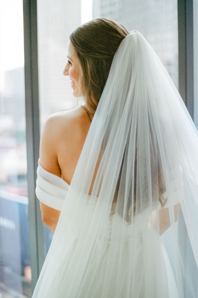 Bride looking over her shoulder with long veil in soft window light captured on film