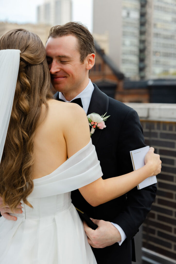 Groom hugging bride on rooftop terrace with Chicago buildings behind them