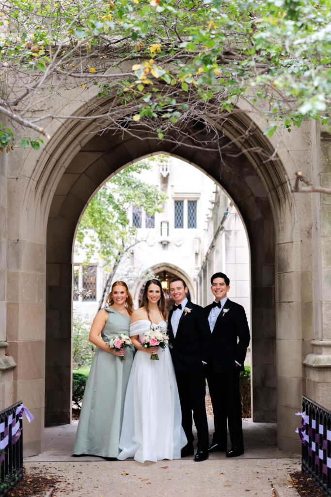 Wedding party standing together beneath stone archway outside the church
