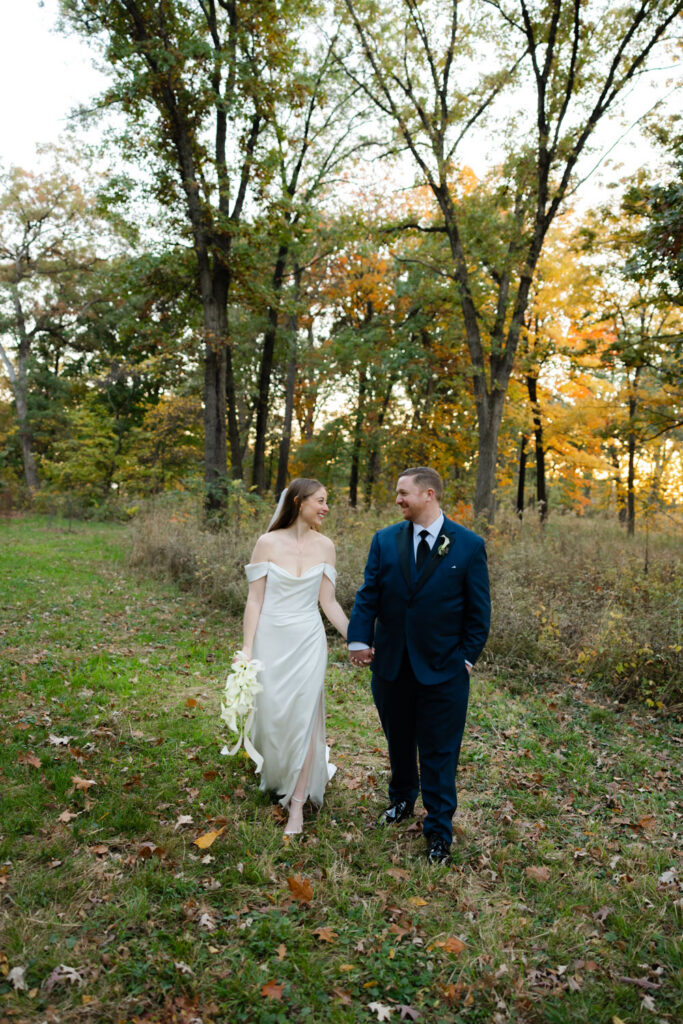 Bride and groom walking together through trees at Morton Arboretum