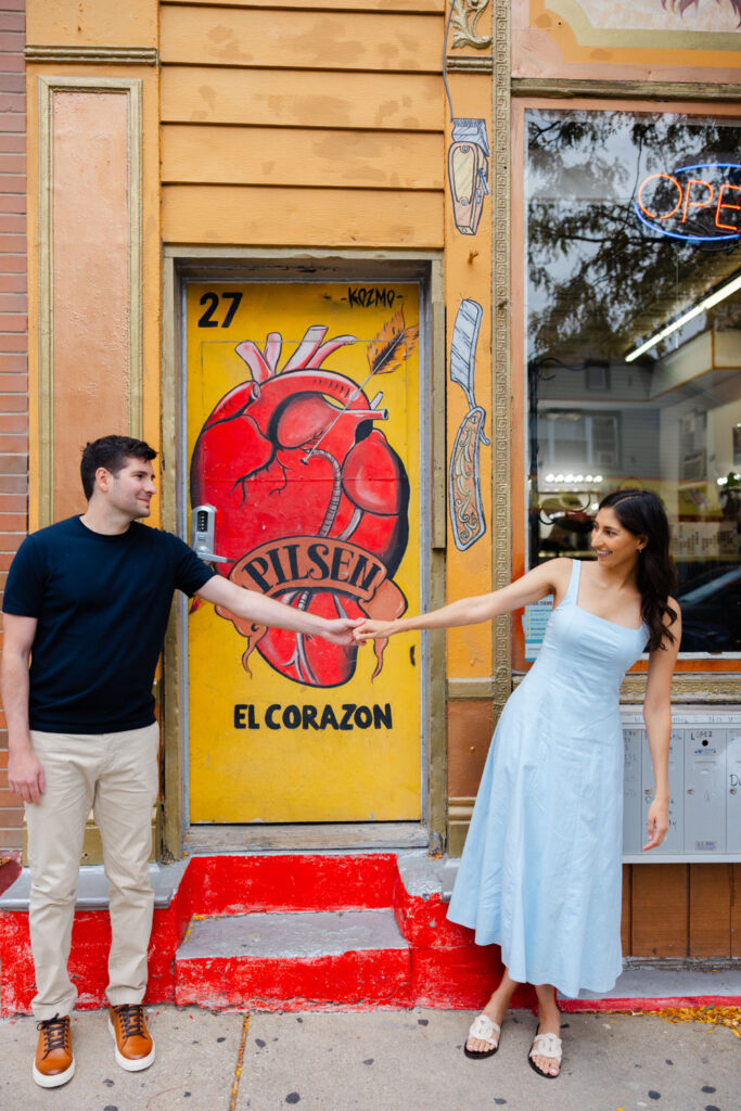 Couple holding hands beside bright yellow Pilsen mural door