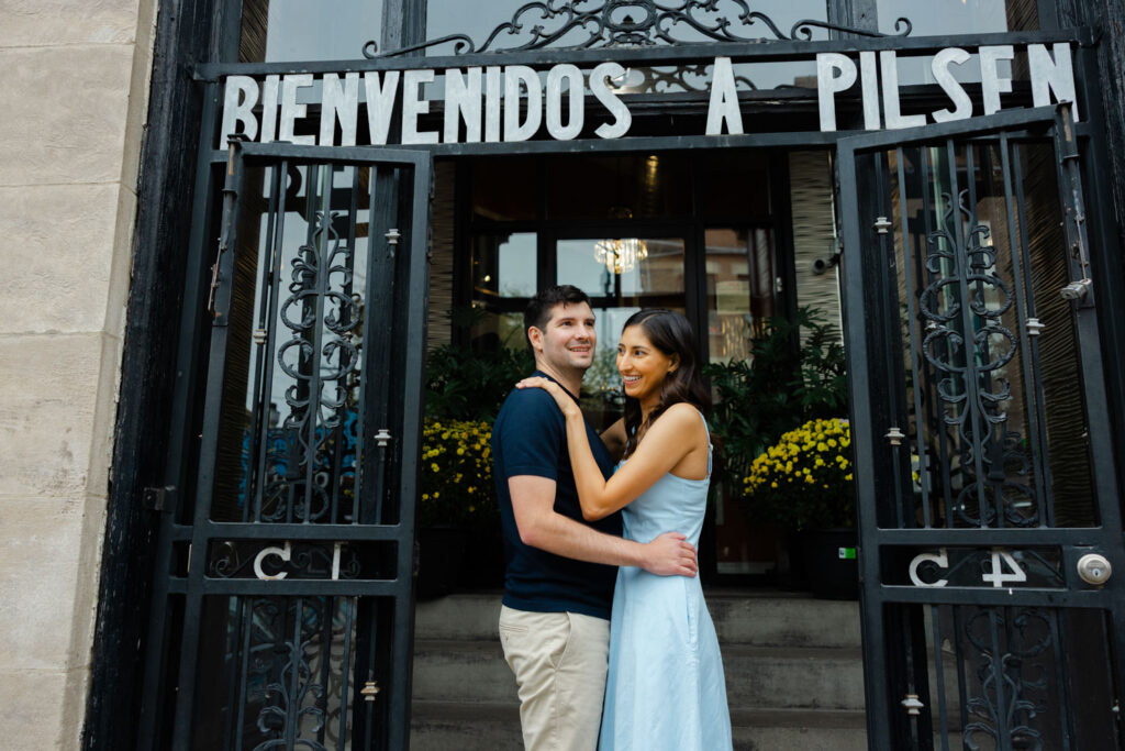 Couple standing beneath Bienvenidos a Pilsen neighborhood entrance sign