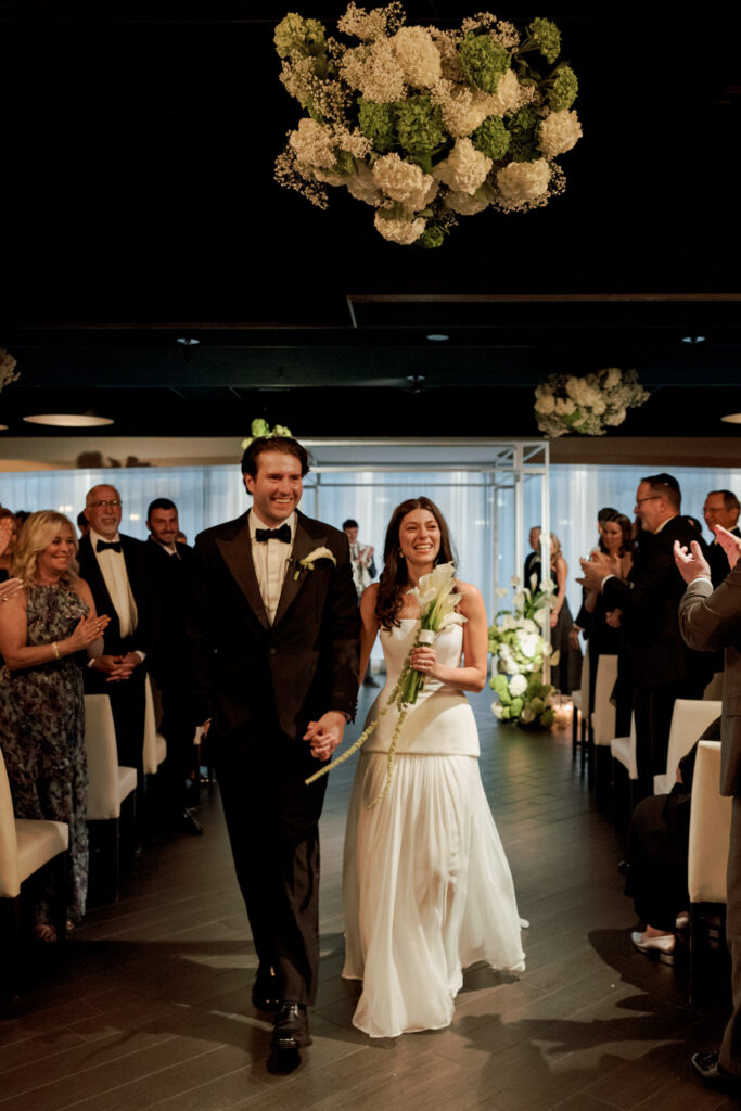 Bride walking down the aisle toward chuppah during modern Chicago wedding ceremony.