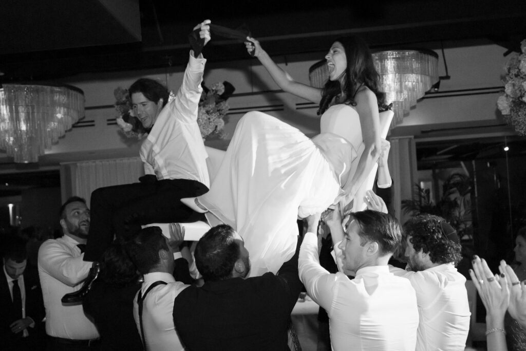 Bride and groom lifted in chairs during the hora at RPM Events wedding reception.
