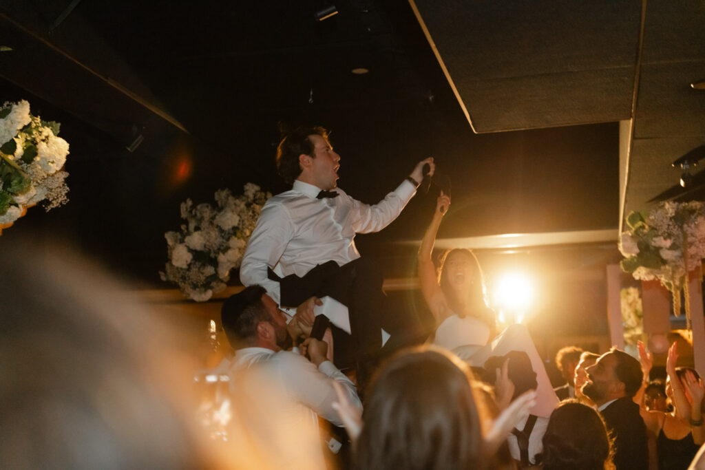 Bride and groom lifted in chairs during the hora at RPM Events wedding reception.