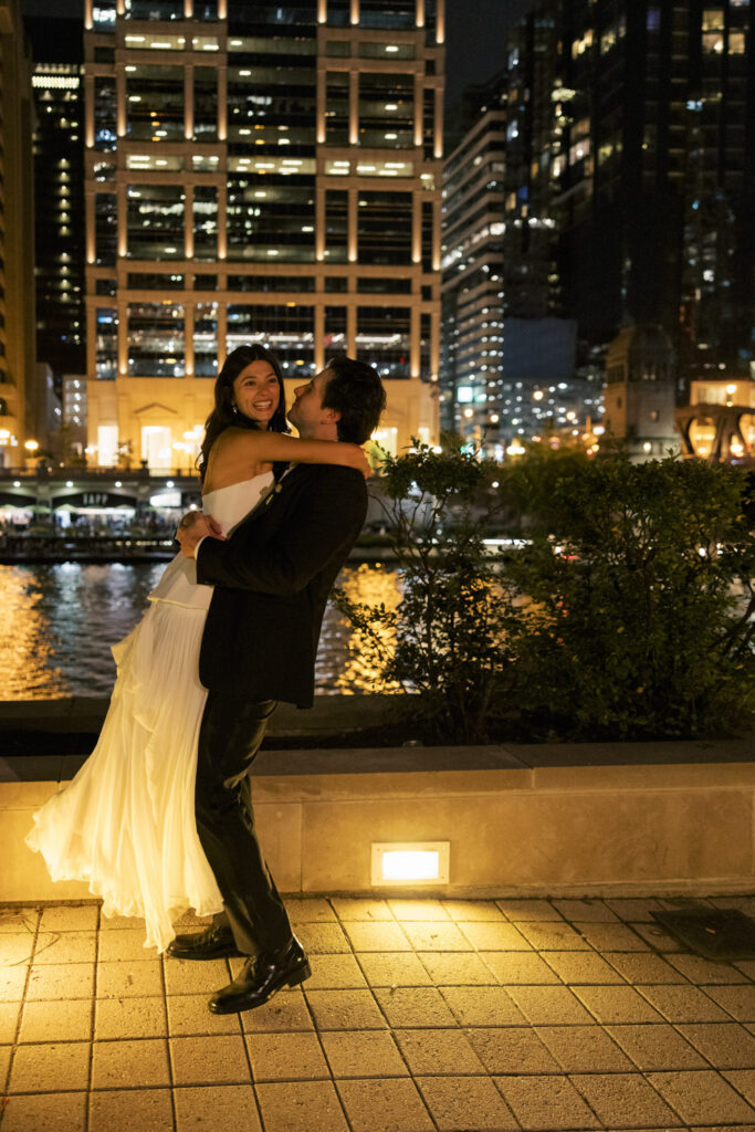 Bride and groom embracing outdoors at night with Chicago city lights behind them.