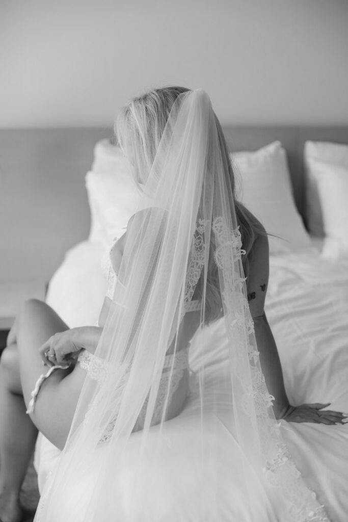 Bridal boudoir session Chicago bride sitting on bed with wedding veil in soft natural light