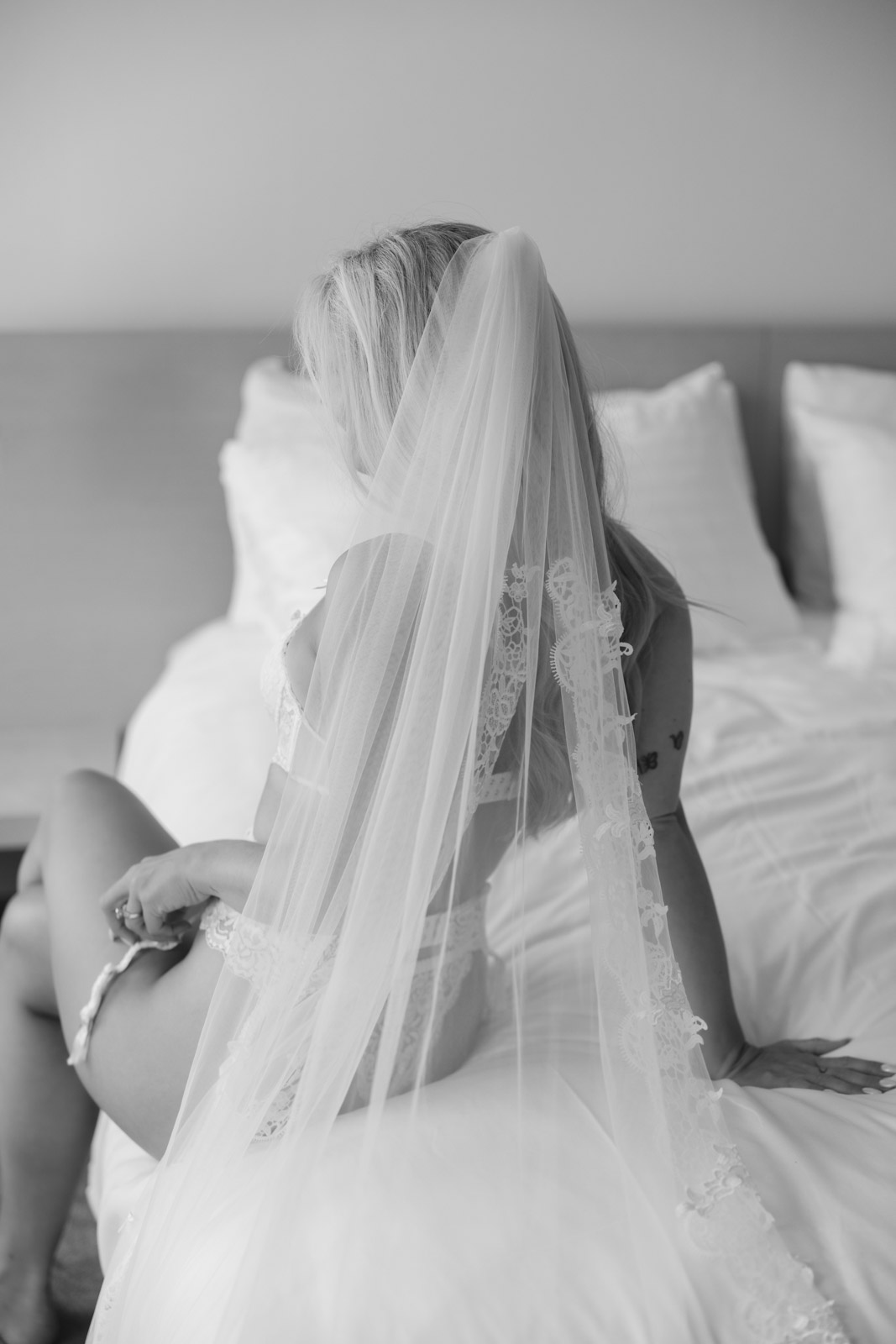 Bridal boudoir session Chicago bride sitting on bed with wedding veil in soft natural light