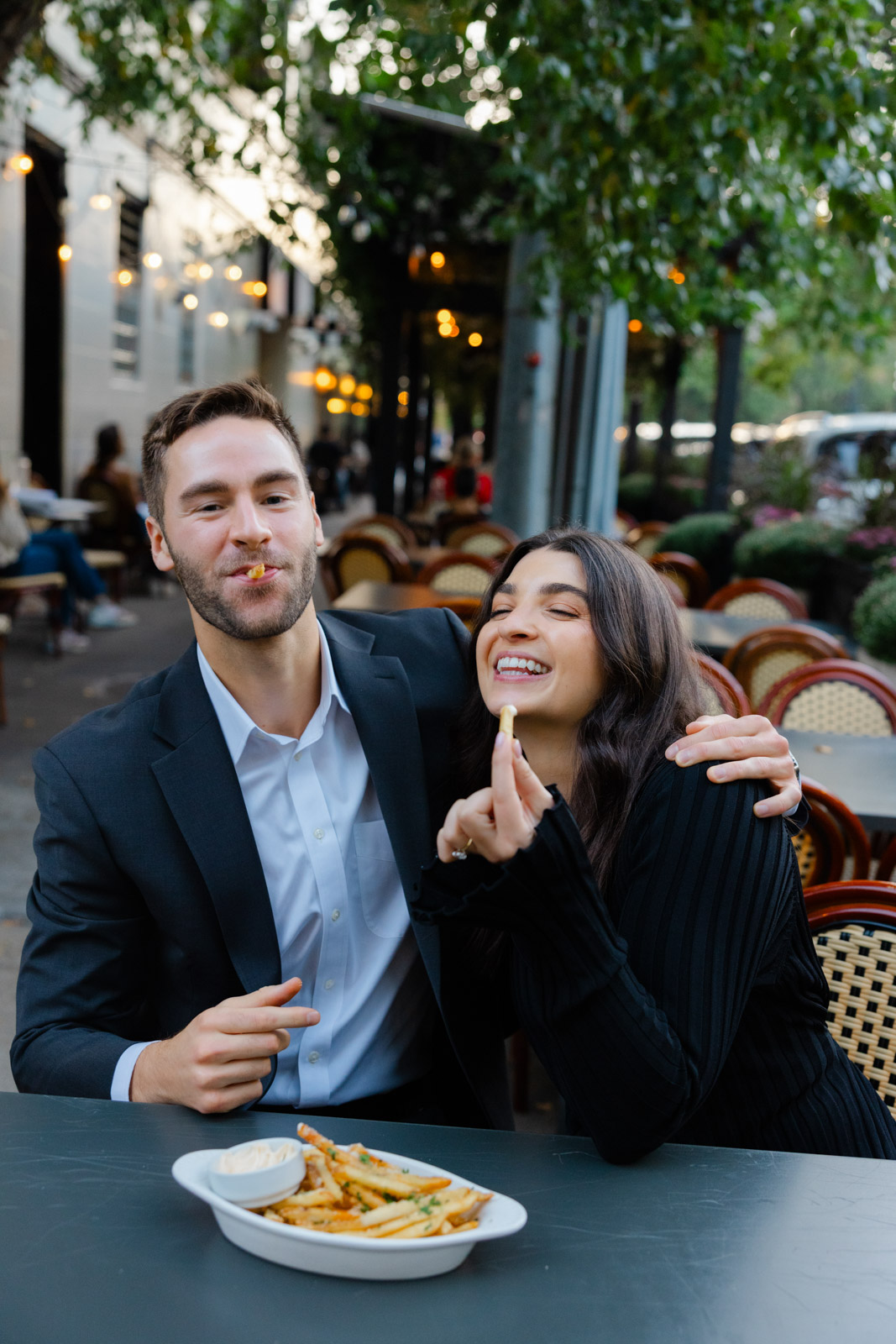 Couple laughing and sharing fries at outdoor restaurant during Lincoln Park Chicago engagement session
