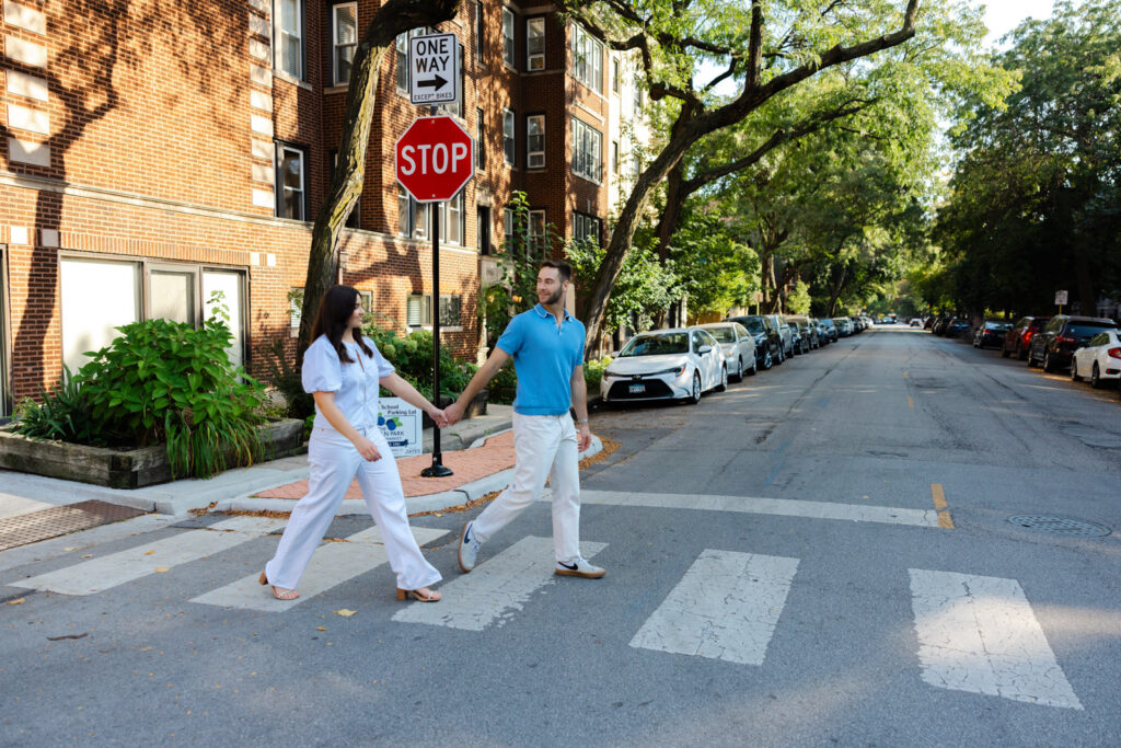 Couple holding hands walking across residential street in Lincoln Park Chicago engagement session