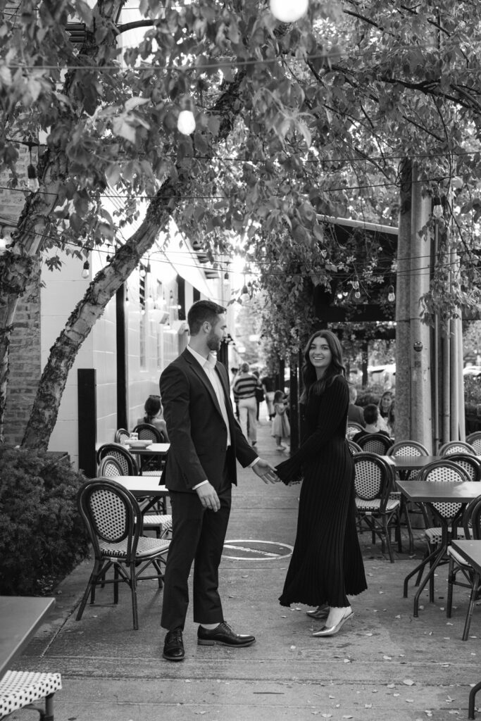Couple holding hands outside neighborhood cafe in Lincoln Park Chicago black and white engagement photo