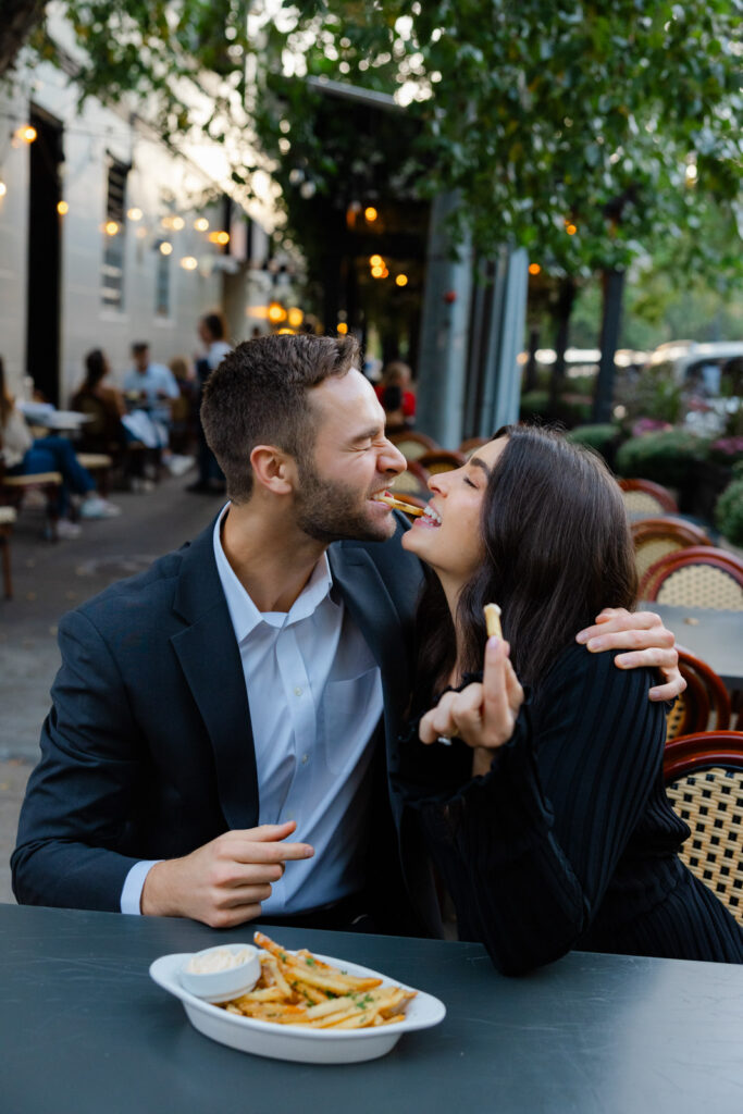 Couple laughing and sharing fries at outdoor table Lincoln Park Chicago engagement session