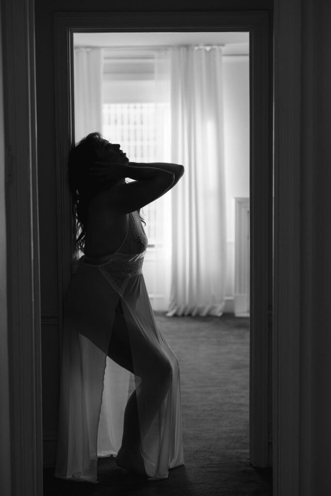 Black and white silhouette of woman arching back near window