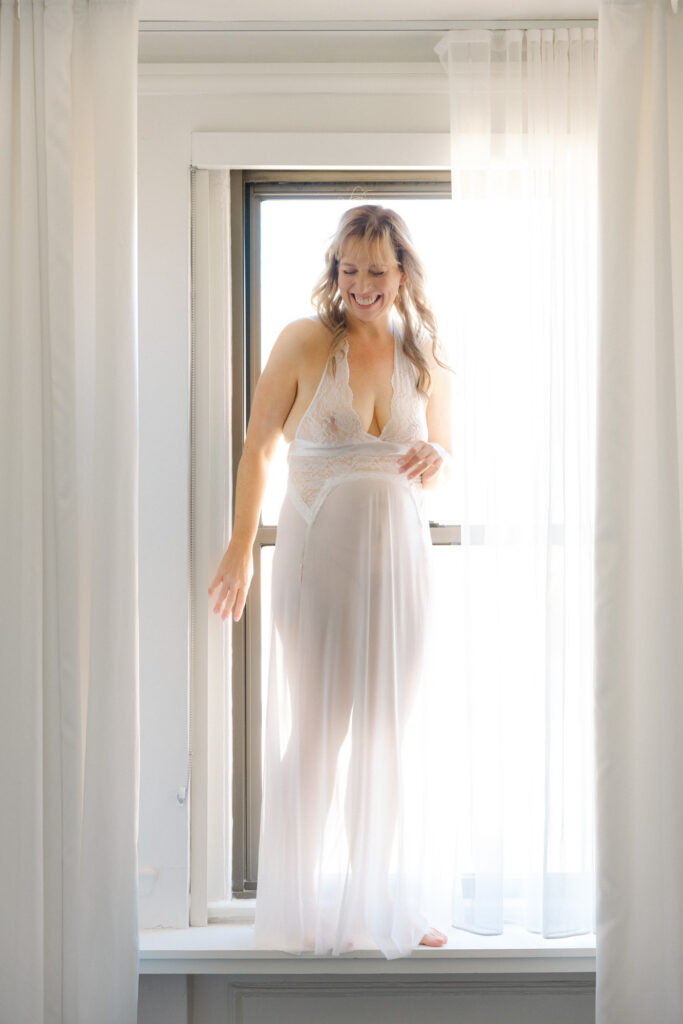 Boudoir photo of woman in sheer robe standing in front of window