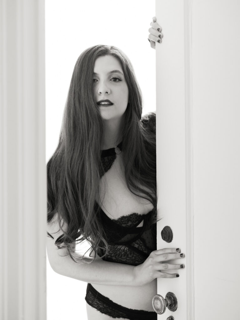 Black and white boudoir portrait of woman in black lace lingerie at doorway