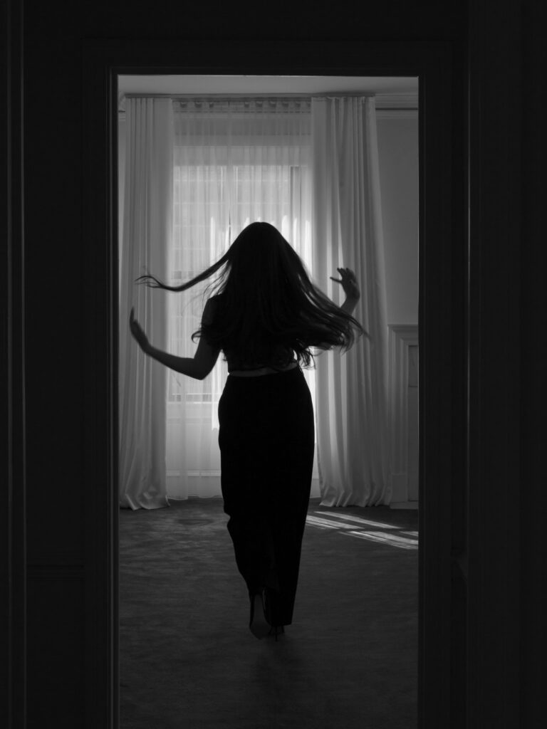 Black and white boudoir silhouette of woman flipping her hair in window light