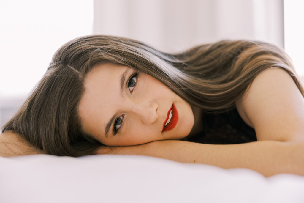 Close-up boudoir portrait of woman with red lipstick lying on white bed