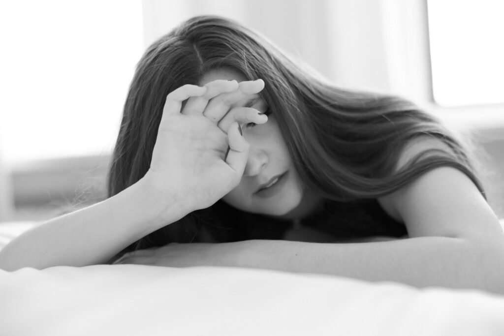 Black and white boudoir photo of woman covering her face while lying on bed