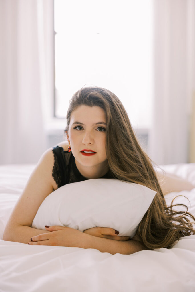 Color boudoir portrait of woman lying on bed holding white pillow