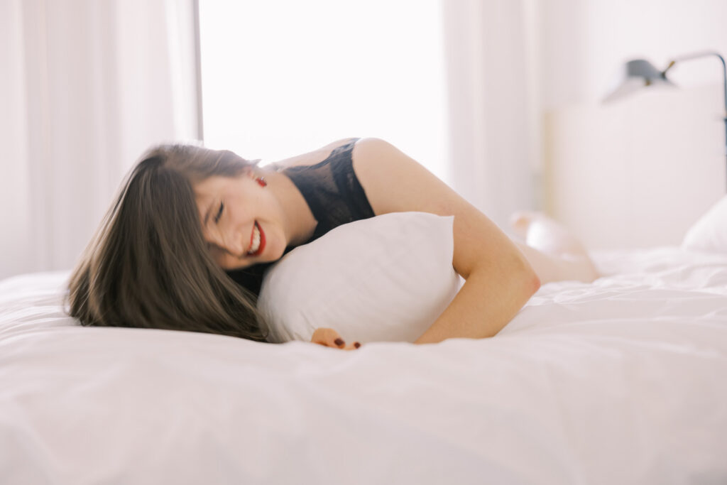Color boudoir portrait of woman lying on bed holding white pillow