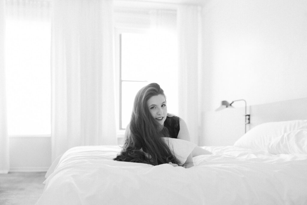 Black and white boudoir photo of woman smiling on bed in lace bodysuit