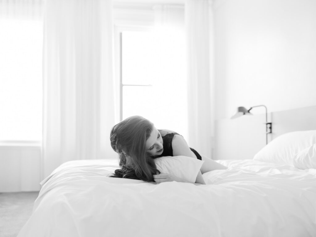 Black and white boudoir portrait of woman sitting on bed with white bedding
